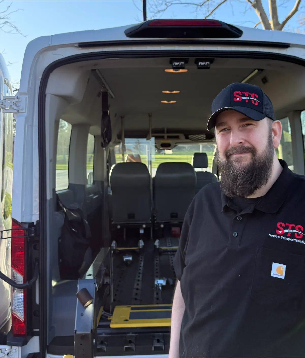 Driver standing beside wheelchair-accessible van with open rear, showcasing safety features and interior space, representing Secure Transport Solutions' commitment to compassionate transportation for individuals with mobility challenges.