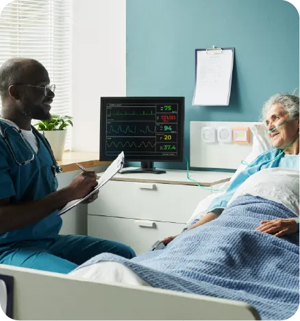 A dark male nurse talking with a very sick bed stricken white elderly woman 
