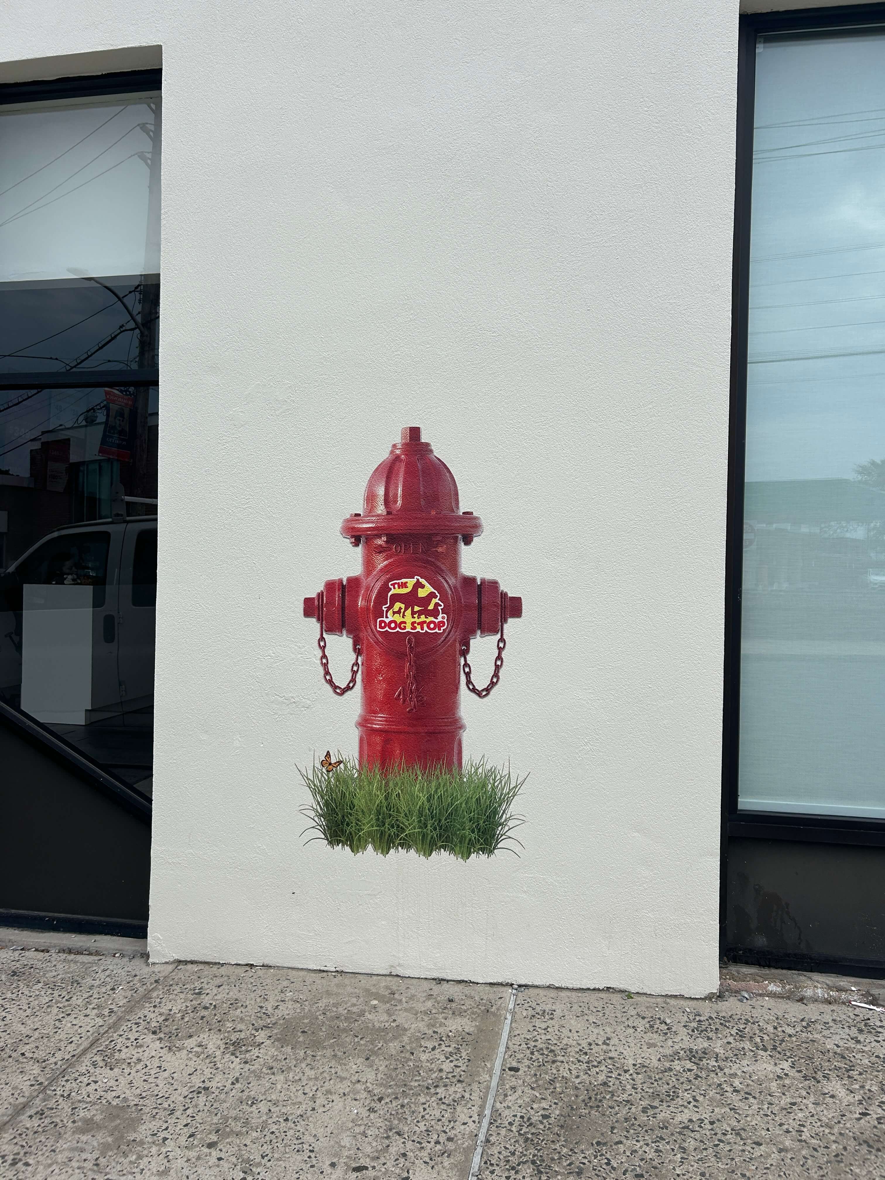 A realistic red fire hydrant mural with "The Dog Stop" logo and grass printed directly onto an exterior textured white stucco wall.