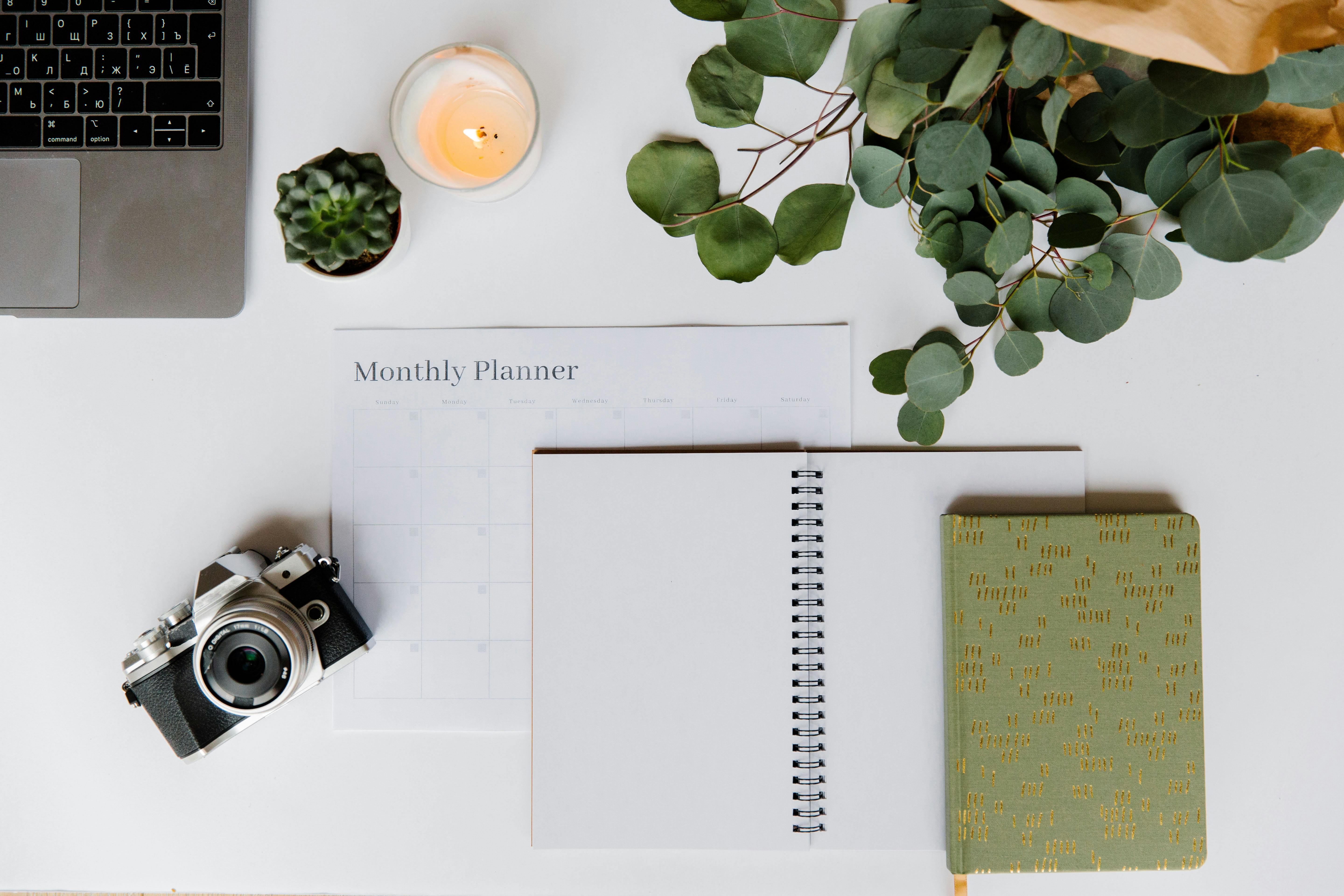 Laptop with monthly planner, notebooks, camera and plant on desk, symbolising brand alignment and structured content planning.