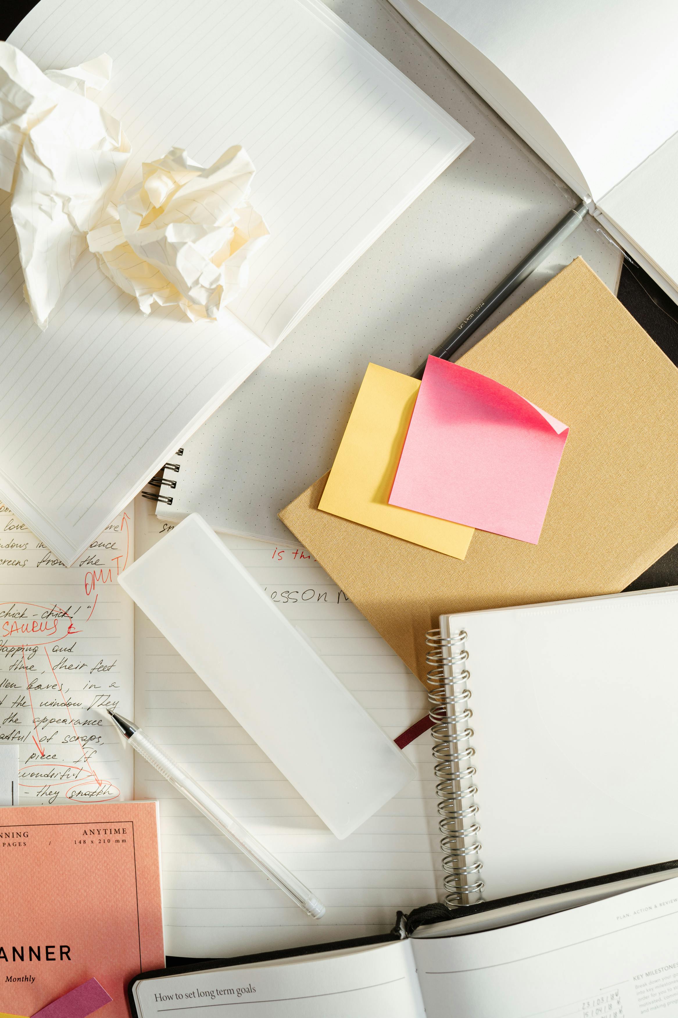 Flat lay of notebooks, planners, sticky notes, and crumpled drafts on a desk, representing scattered ideas and lack of structured brand direction.