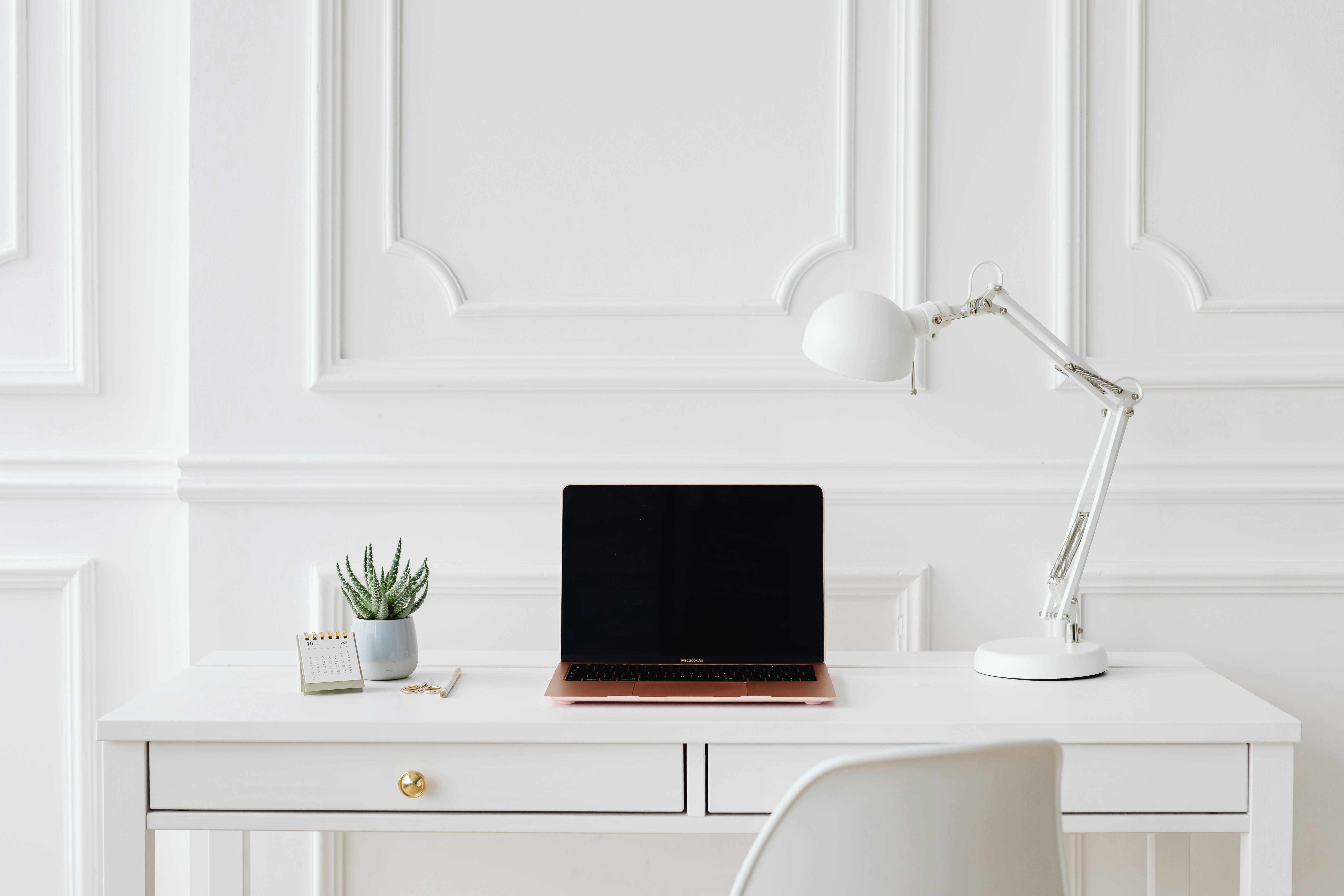 Clean white home office desk with an open laptop, arc lamp and small plant, representing a structured and considered working environment.