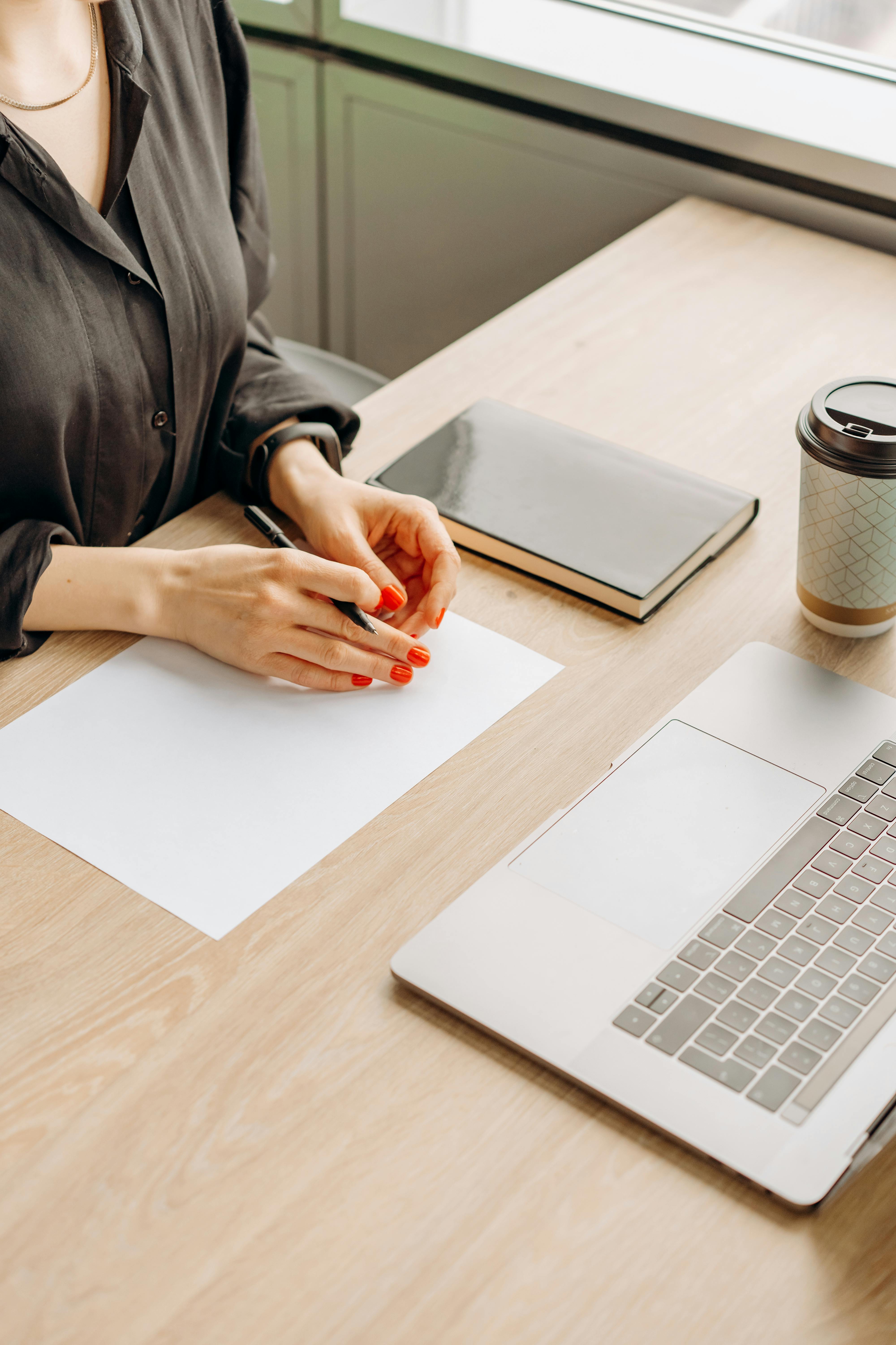 Professional pausing at a blank page with laptop and notebook on a wooden desk, representing undocumented brand standards for an established service business.