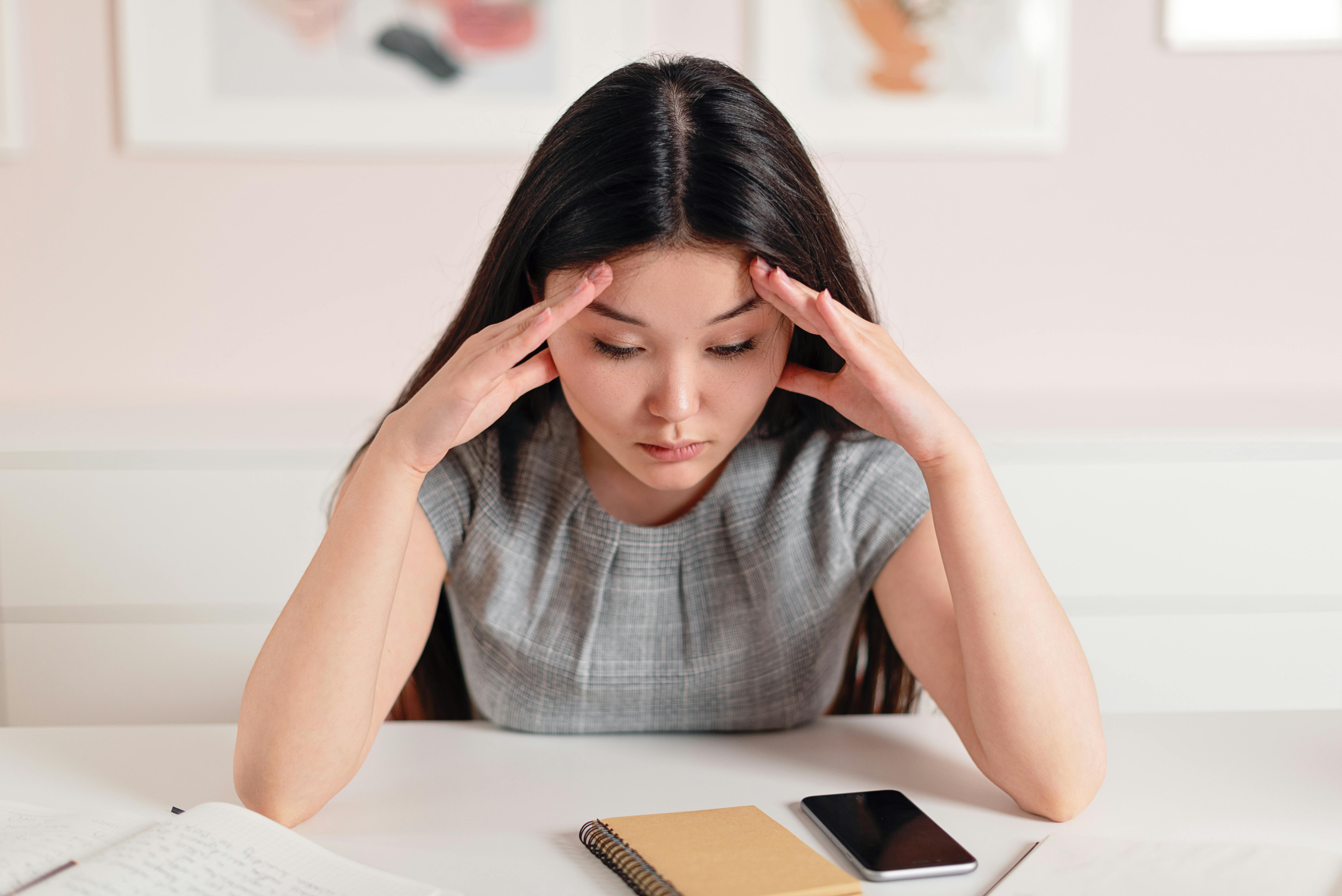 Woman with fingers on temples Female service business owner overwhelmed at her desk without a marketing funnel system in place