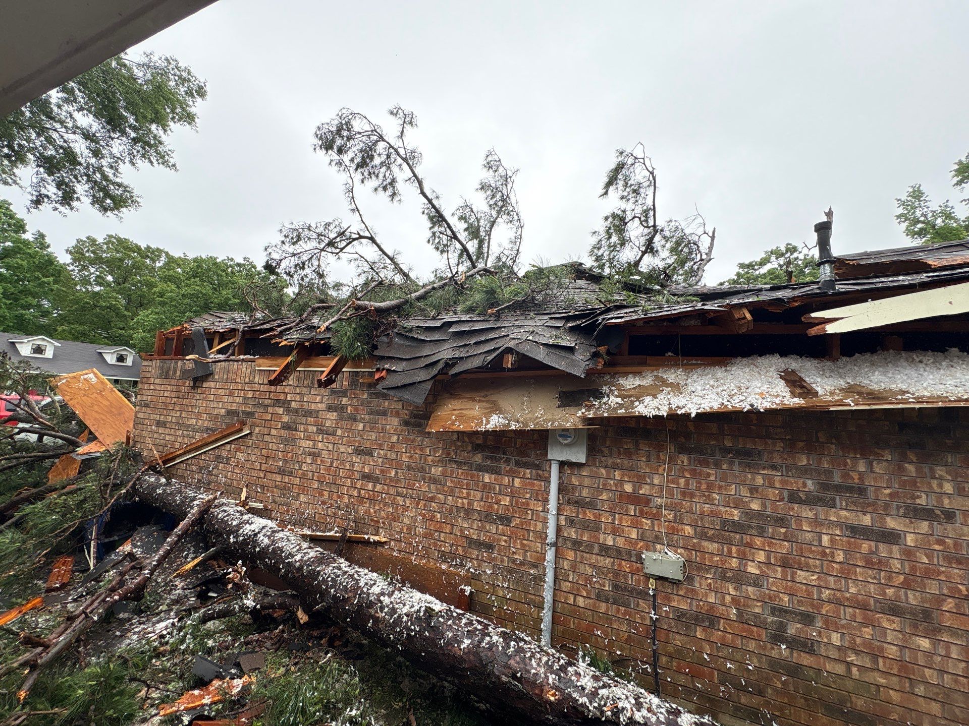 Close-up of fallen tree crushing brick home roof after storm — storm damage contractors serving Bossier City and Shreveport