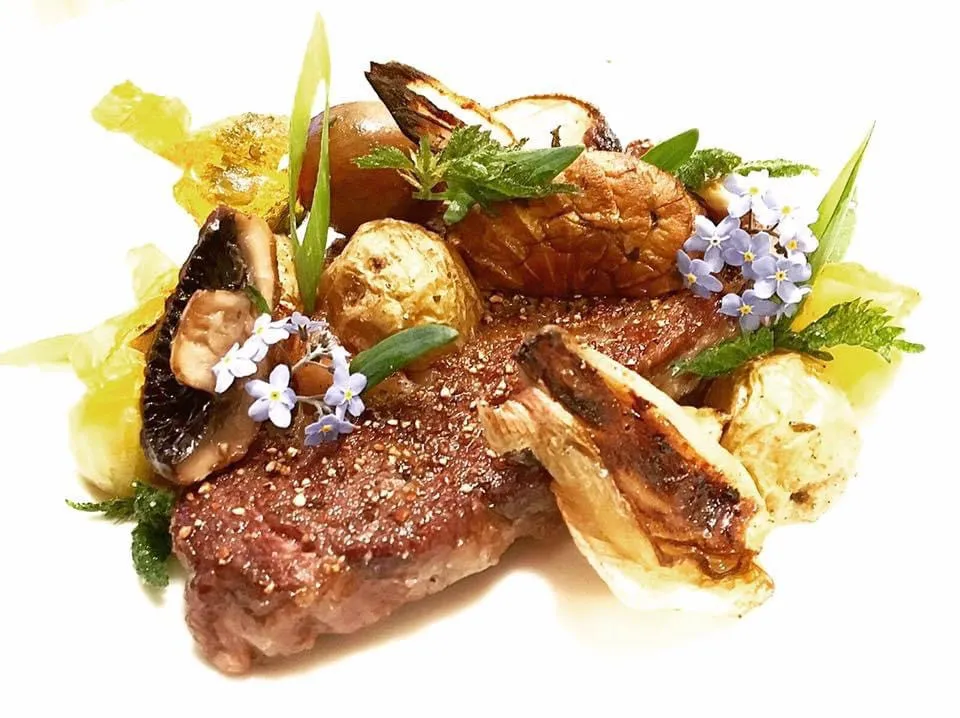 A plated steak with roasted potatoes and greens