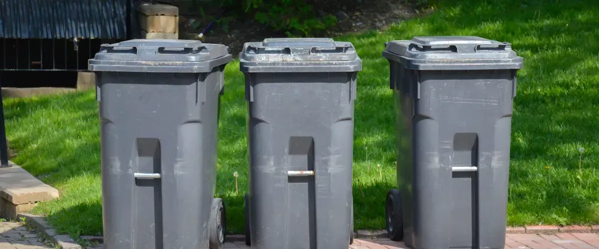 Three gray trash bins lined up on a clean brick pathway