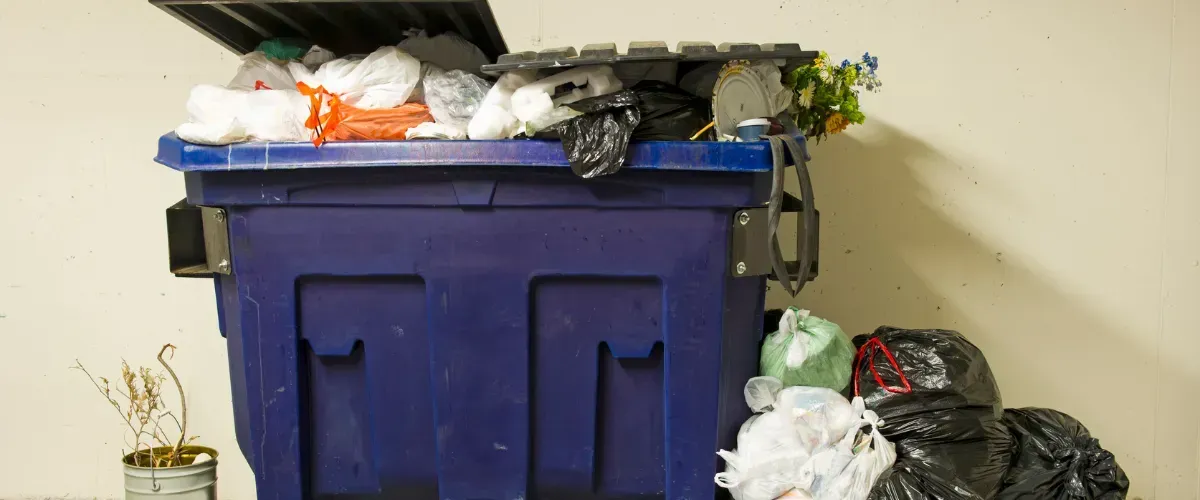 Overflowing blue dumpster filled with garbage bags, showing need for cleaning service