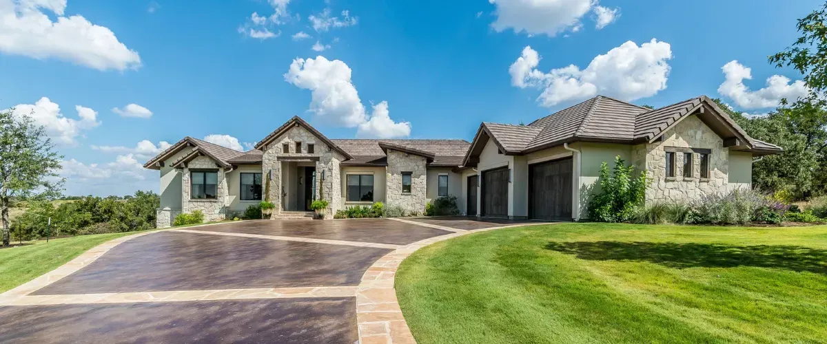 Modern stone house with a curved driveway and well-maintained lawn under a blue sky