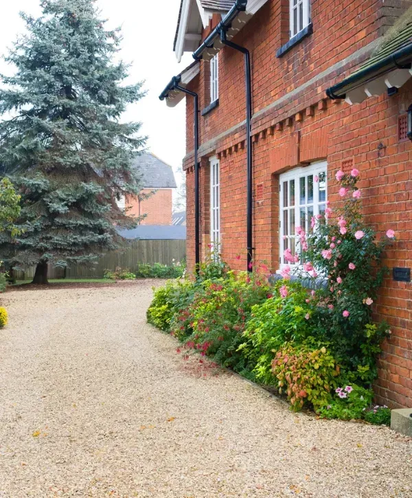 Traditional red brick house with a gravel driveway and blooming flower garden along the front