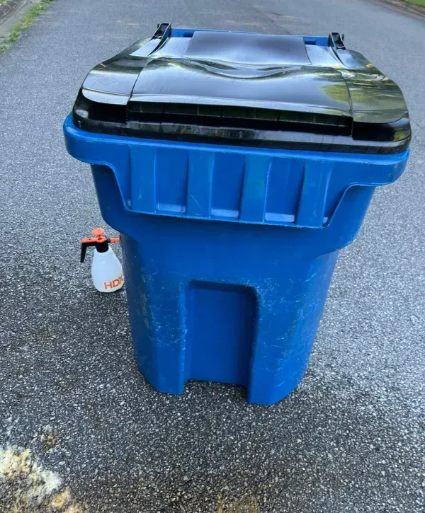 Blue trash bin prepared for cleaning service with spray bottle beside it.