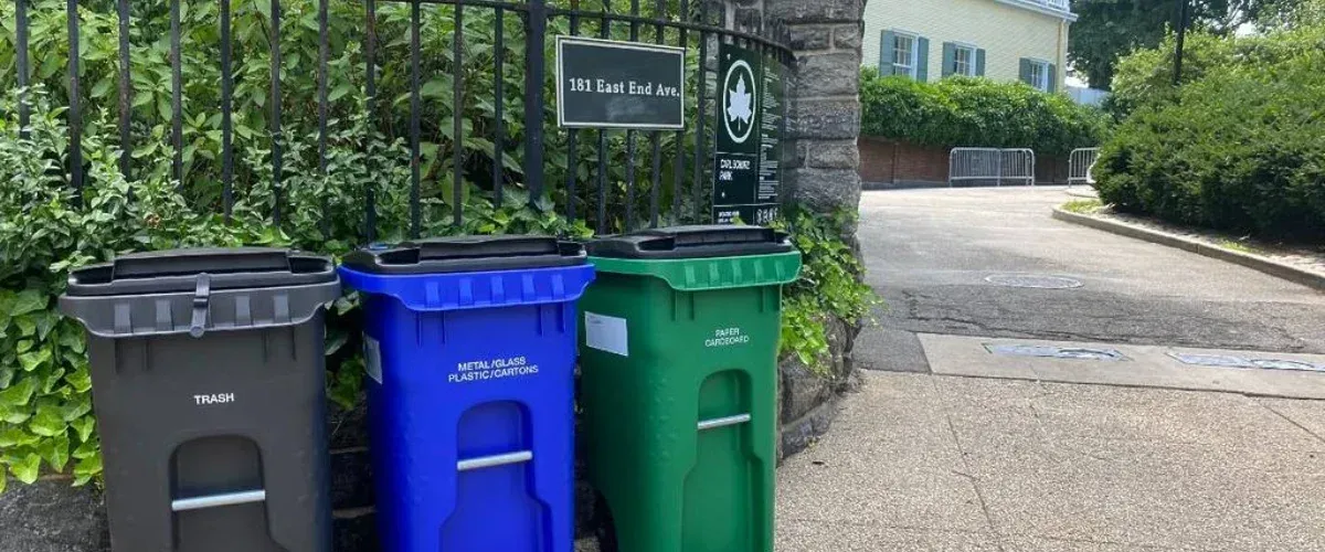 Residential trash, recycling, and compost bins placed curbside in front of a property. 