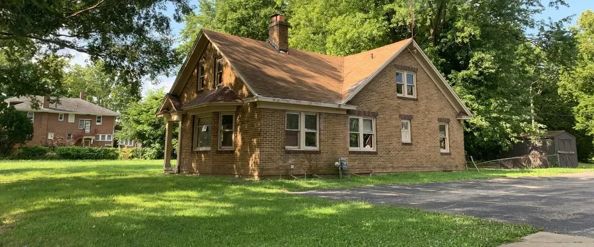 Charming vintage brick house with gabled roof surrounded by green lawn and trees