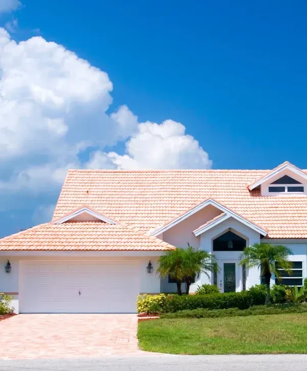 Beautiful Alabama-style house with terracotta roof, palm trees, and sunny blue sky backdrop.