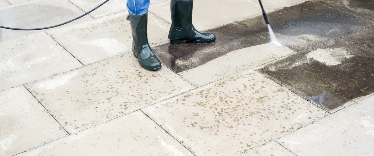 Worker using high-pressure washer to clean dirty patio tiles with visible before and after results