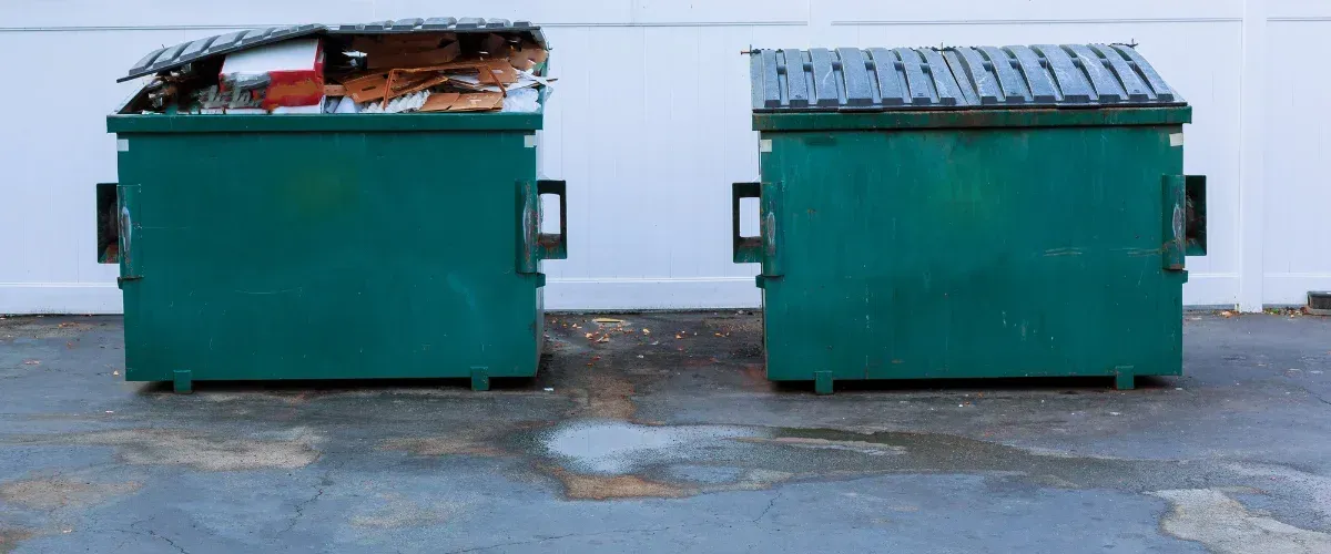 Trash dumpster next to stacked cardboard boxes for recycling and disposal