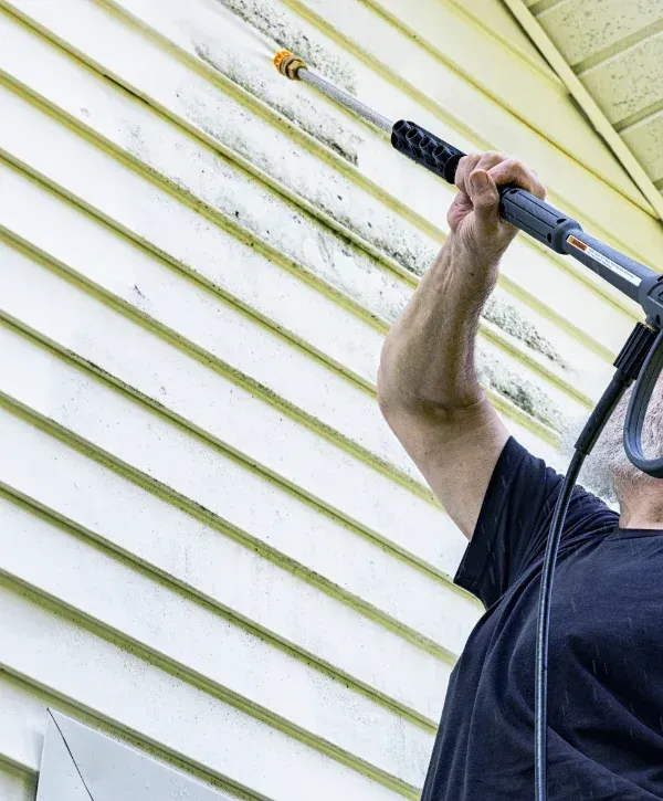 echnician pressure washing modern home exterior with commercial equipment