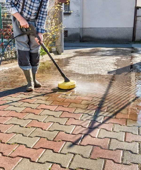 Worker pressure washing brick paver driveway surface
