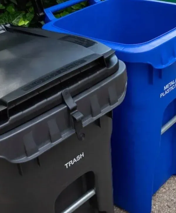A close-up view of a black trash can marked 'TRASH' next to a blue recycling bin for metal and plastic.