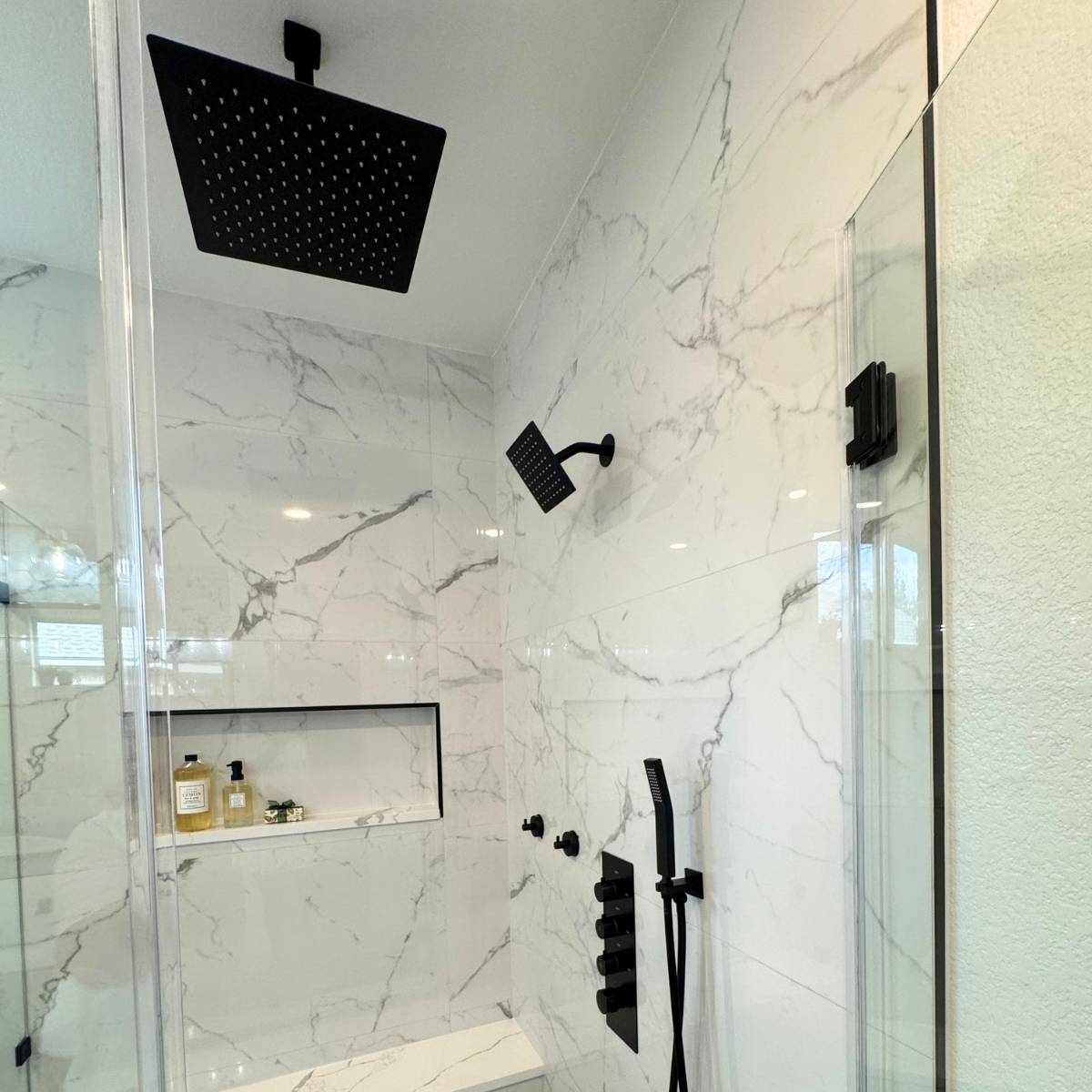 Spa-style walk-in shower after bathroom renovation with frameless glass, tile niche & black fixtures