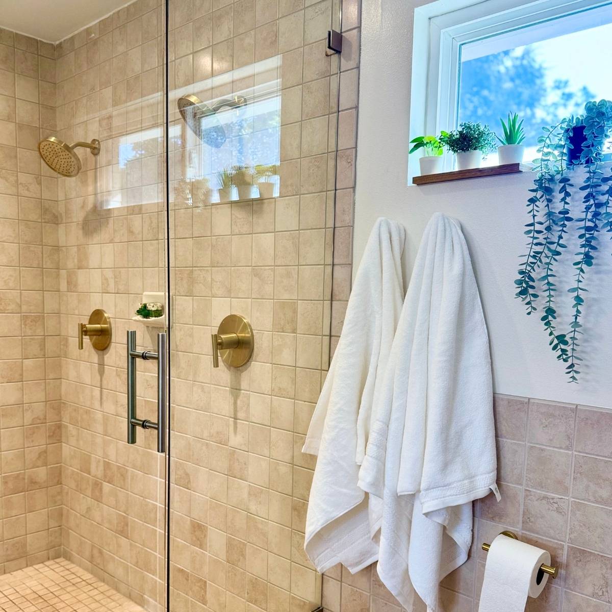 Spa-style walk-in shower after bathroom renovation with frameless glass and window and modern gold fixtures”