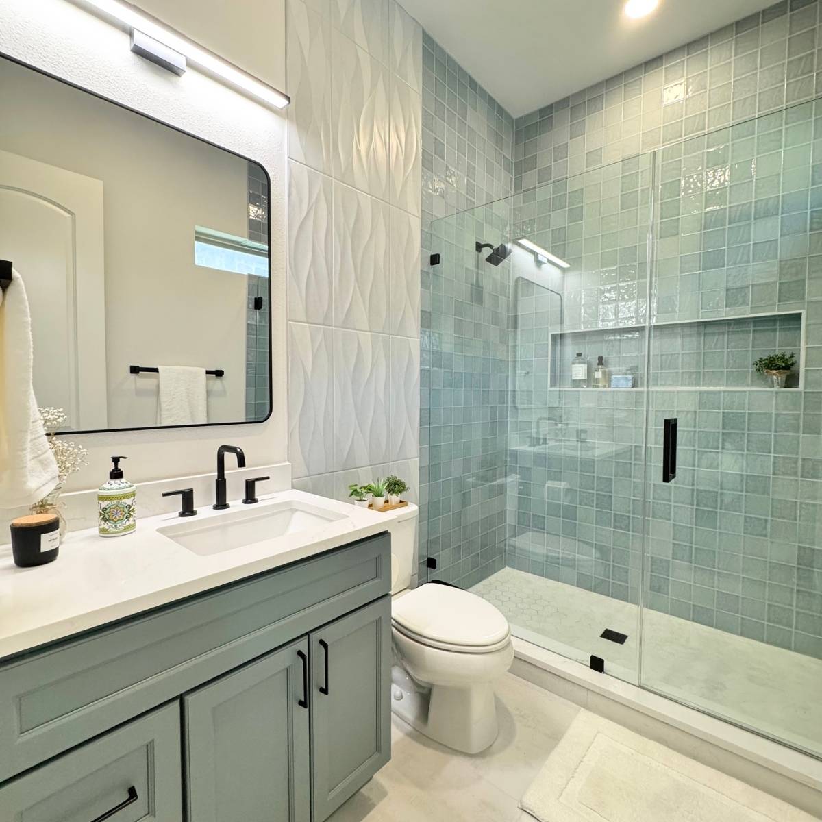 Contemporary bathroom after Jack & Jill remodel featuring custom blue tile, white tile, glass shower, and black fixtures