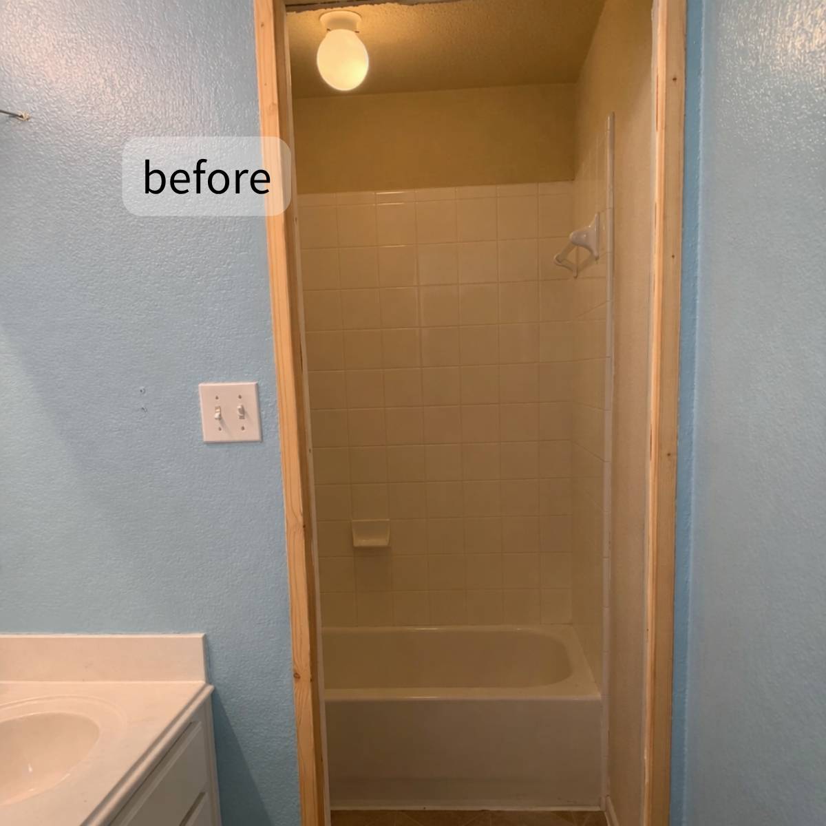 Narrow bathroom before upgrade with walled-in shower and yellow lighting