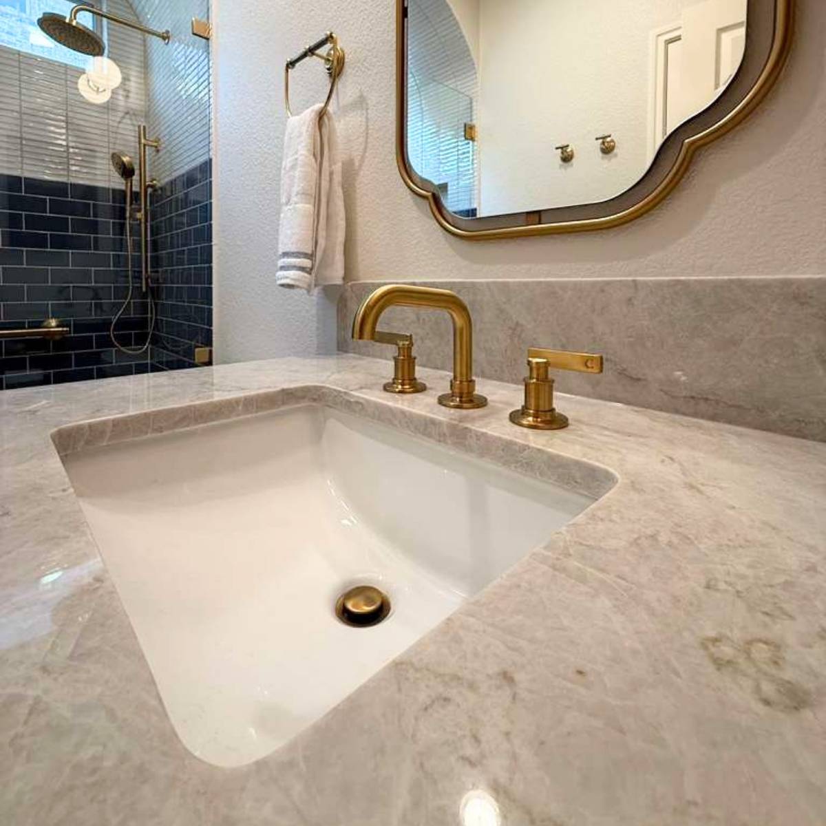 Luxury bathroom vanity remodel in Austin featuring quartz countertops, brushed gold faucet and hardware, undermount sink, custom mirror, and a spa-inspired walk-in shower with deep blue subway tile and frameless glass by ATX Custom Remodel