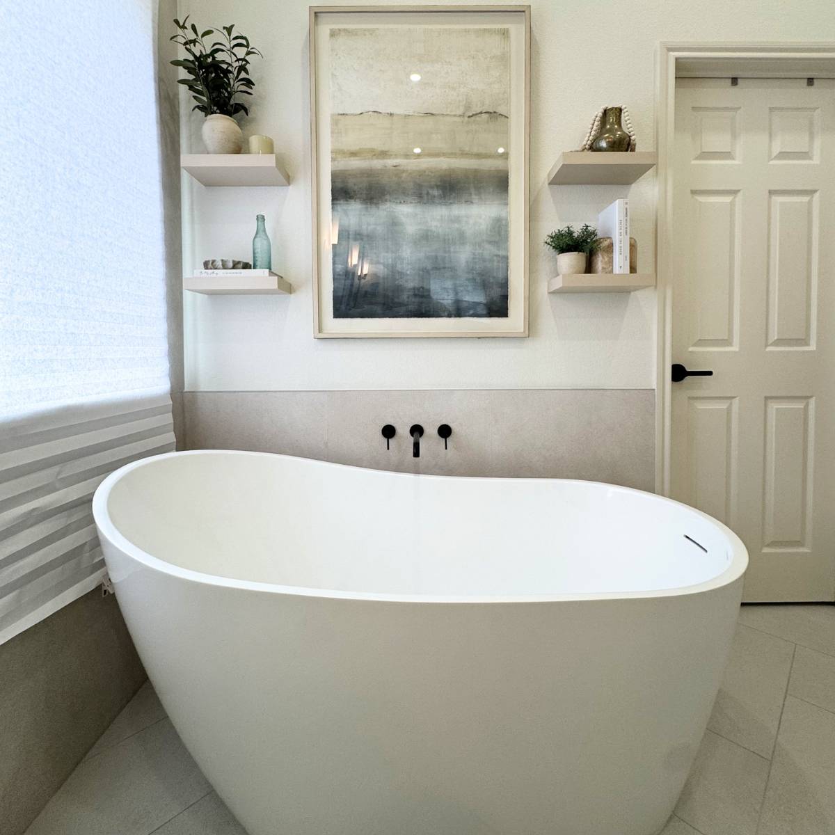 Luxury primary bathroom remodel in Cedar Park TX featuring a custom white freestanding soaking tub, matte black fixtures, custom floating shelves and light porcelain tile by ATX Custom Remodel.