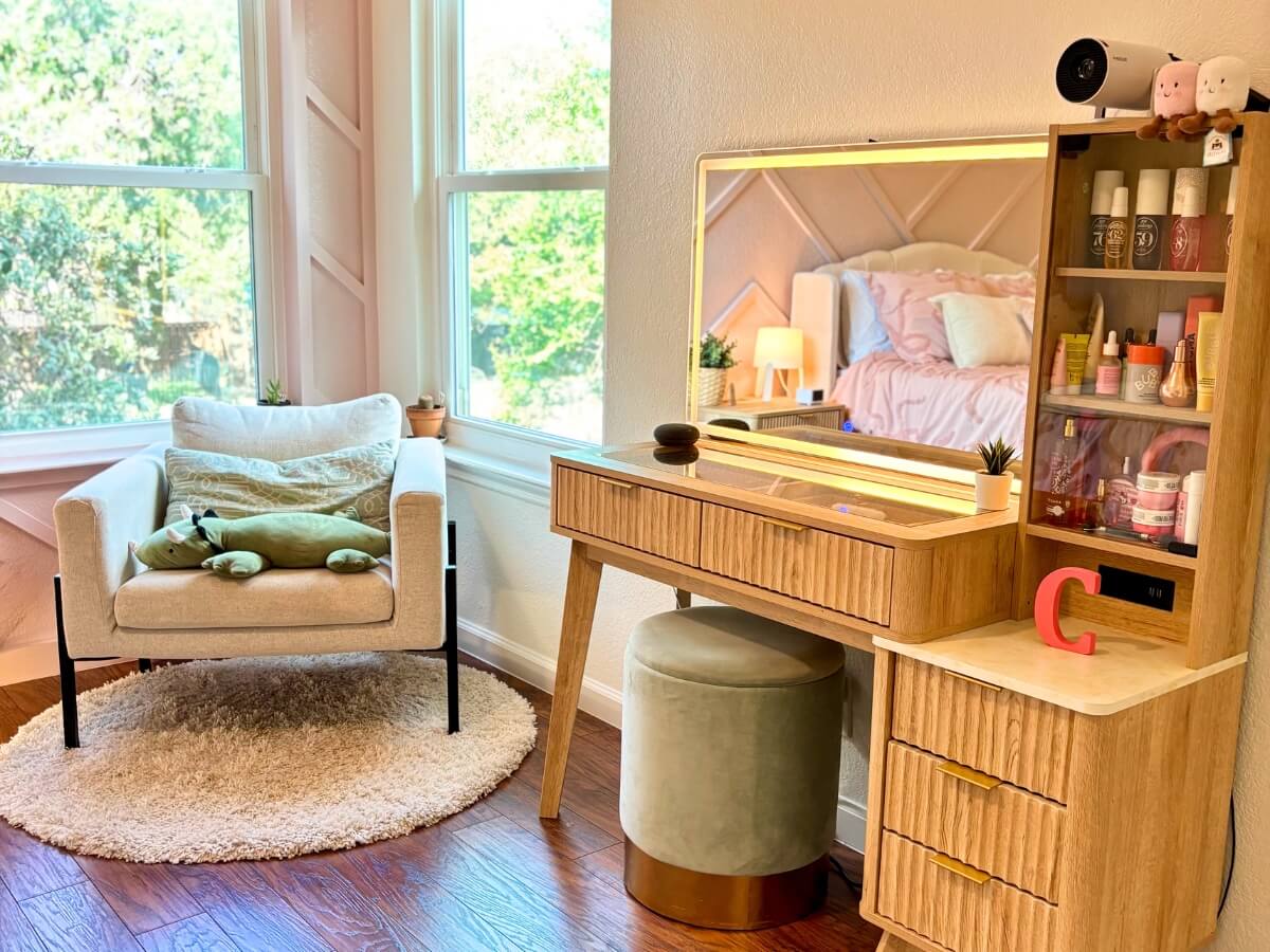 Custom fluted wood makeup vanity desk with LED mirror and green velvet stool next to a cozy reading chair.