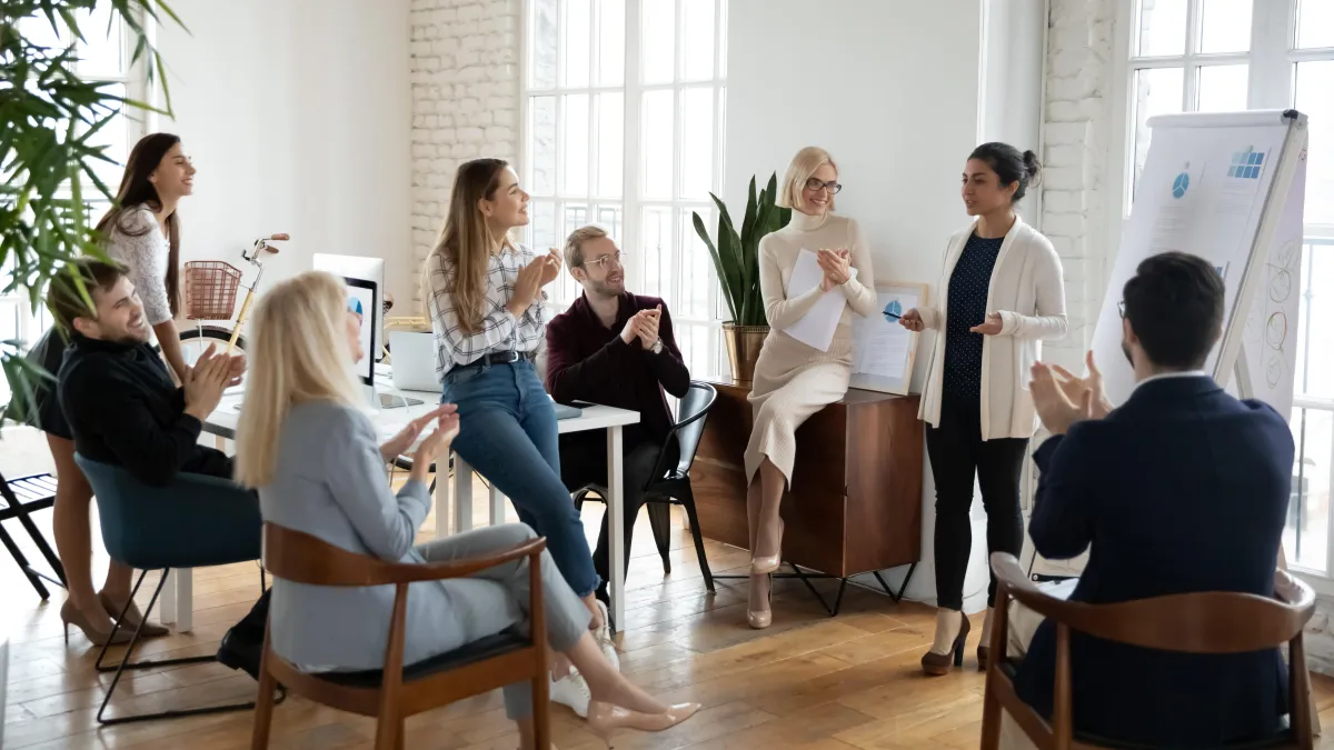 A small group of people are listening to  lady in front of a flip chart, she is speaking