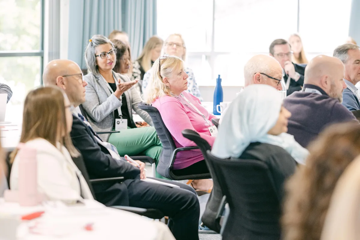 A room of people facing a trainer who is out of shot. One person is asking a question.
