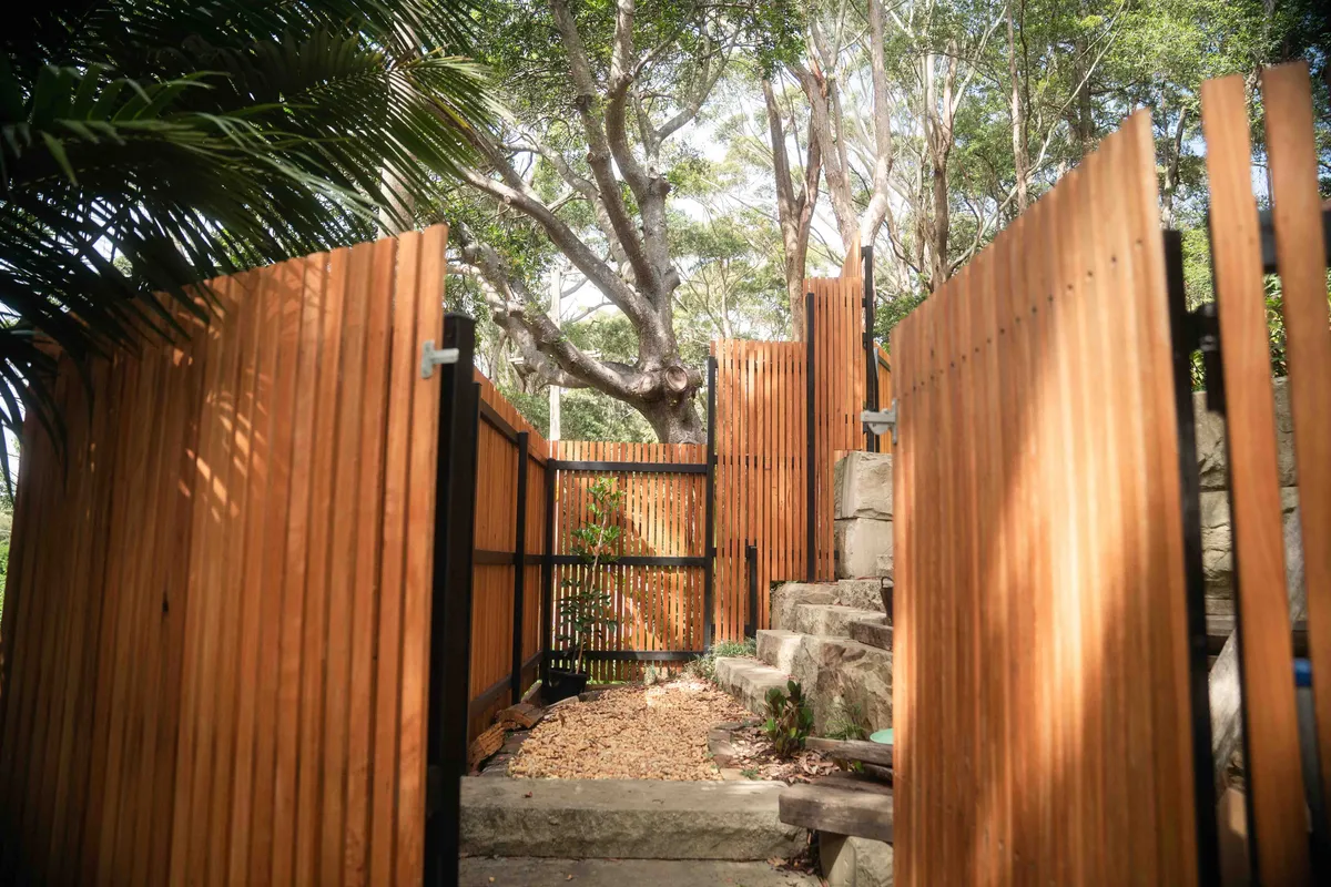 Tall hardwood batten gate among palms and sandstone