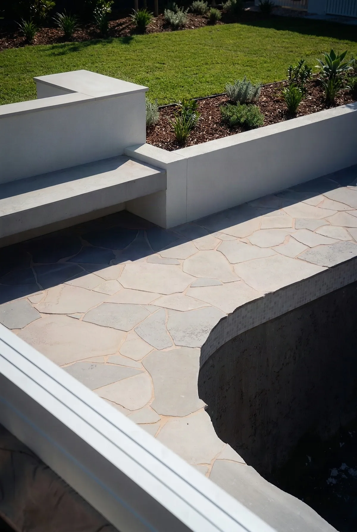 Crazy-paved natural stone terrace beside a rendered seat wall and pool edge
