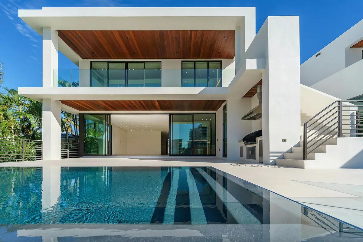 Long concrete pool with a tiled floor in front of a modern two-storey home