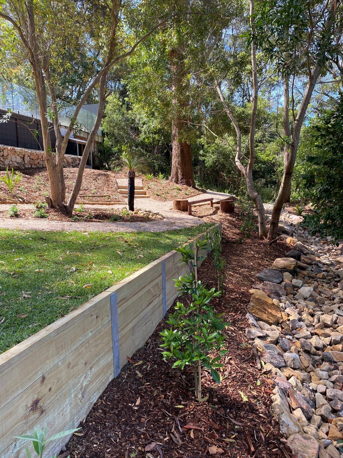 Timber sleeper retaining wall beside a dry creek bed and native planting