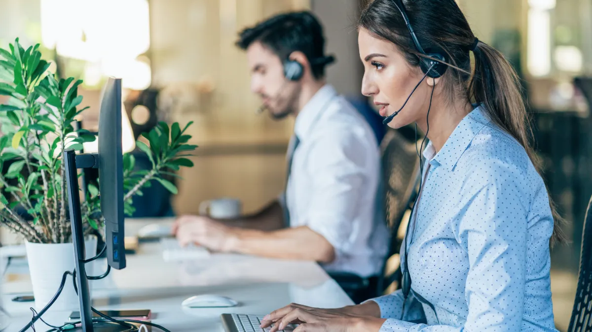 A diverse group of real estate professionals gathered around a table, discussing documents and smiling. The office is decorated with EXIT Elite Realty branding, and the atmosphere is collaborative and supportive. 3:2 aspect ratio.