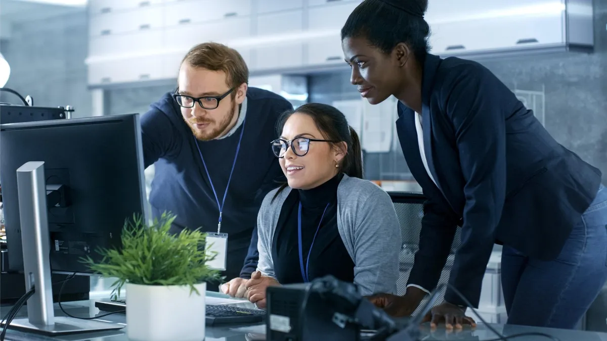 Three office coworkers reviewing security guidance together at a monitor during employee cybersecurity training
