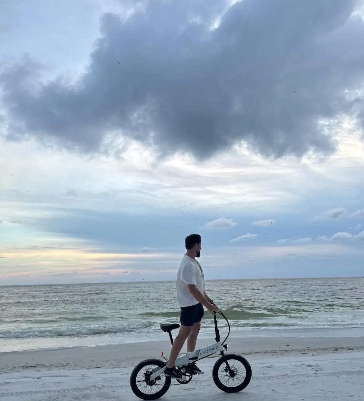 Man standing on a Bosco Rentals electric bike on the beach in Sarasota, FL, with the ocean in the background.