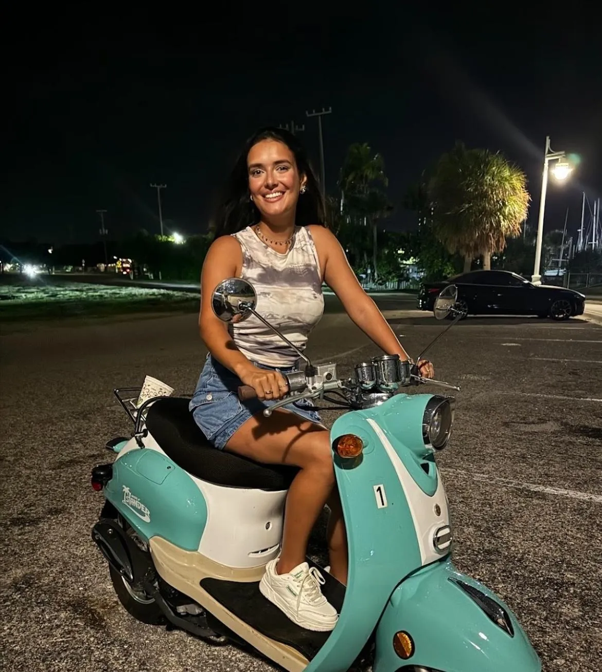 Woman smiling on a Bosco Rentals one-seater scooter in Sarasota, FL, enjoying a sunny beach day.