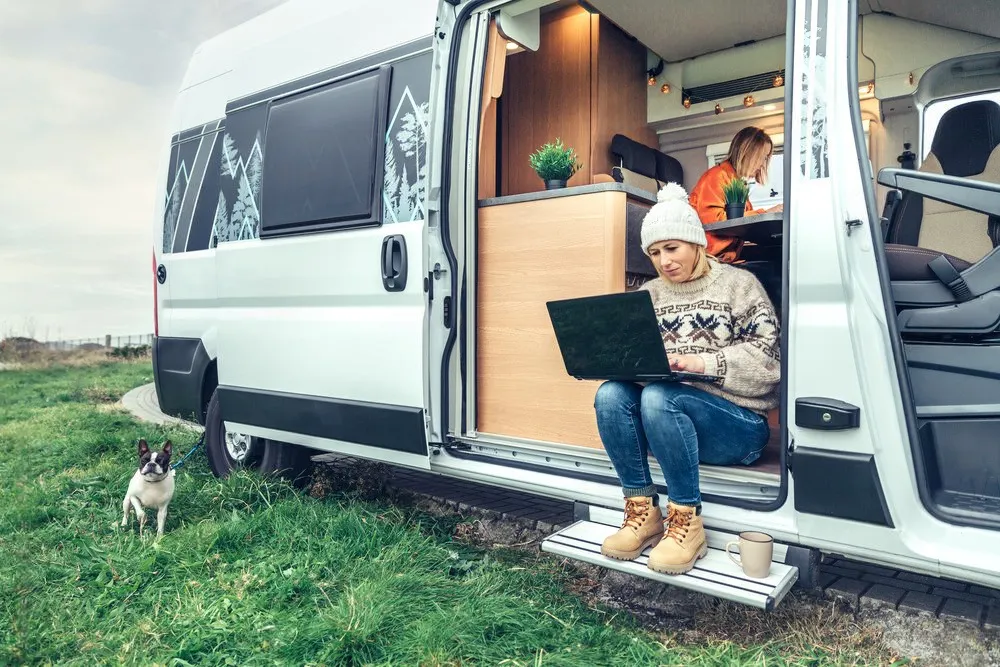 Image of a woman sitting in the door of her  online RV registration shopper. Searching for a Montana llc RV registration service on a black laptop. - Dirt Legal