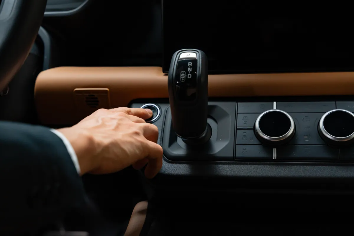 A photograph of a man in a suit pushing the start button of a land rover SUV.