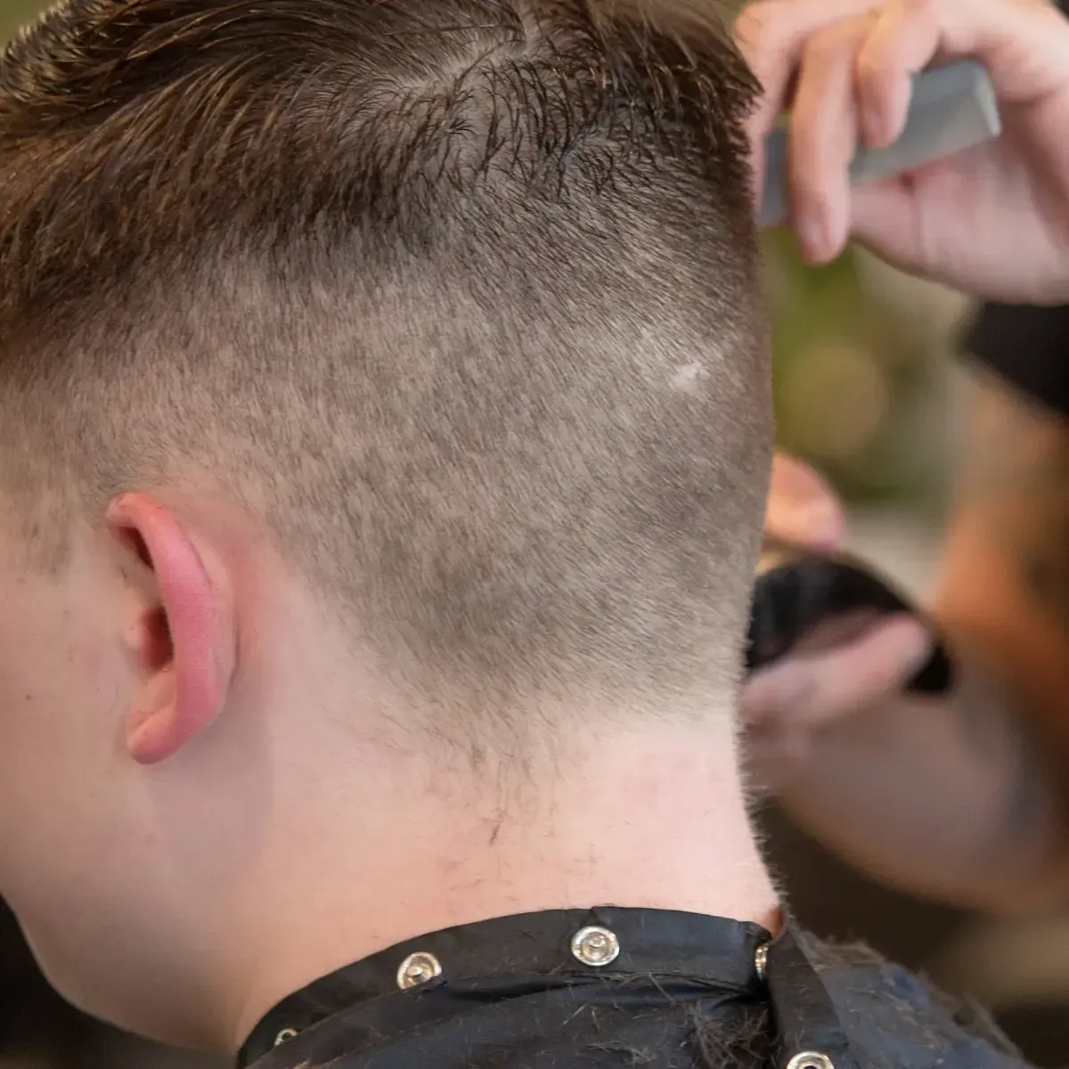 Barber at Scuttlebutt Barbershop in Portsmouth, NH using clippers to shape a clean buzz cut for a client in a black cape.