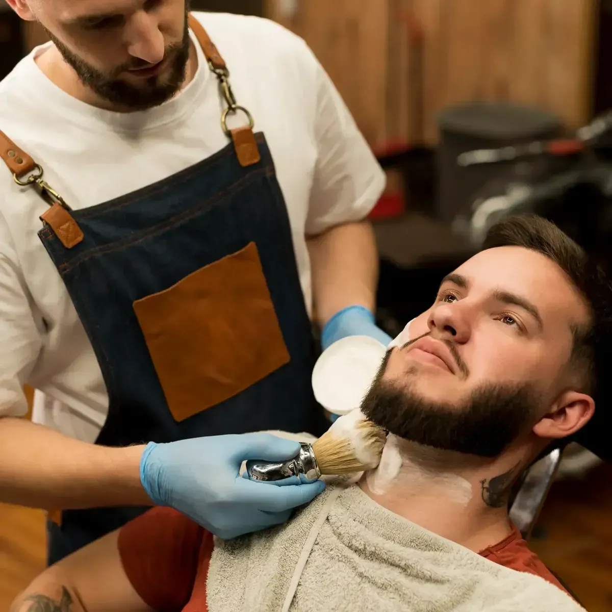 Barber at Scuttlebutt Barbershop in Portsmouth, NH applying hot lather to a client’s neck before a traditional straight razor shave.