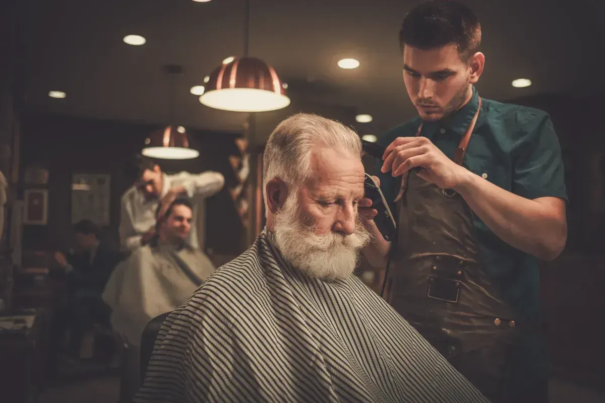 Barber at Scuttlebutt Barbershop in Portsmouth, NH giving a haircut to an older gentleman in a warm, vintage-style barbershop.