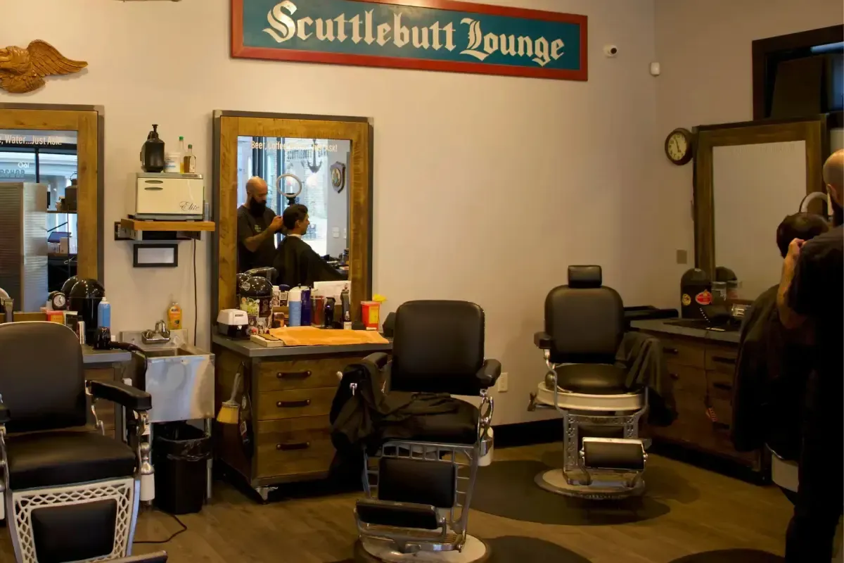 Interior of Scuttlebutt Barbershop with barber chairs, mirrors, and a barber cutting a client’s hair