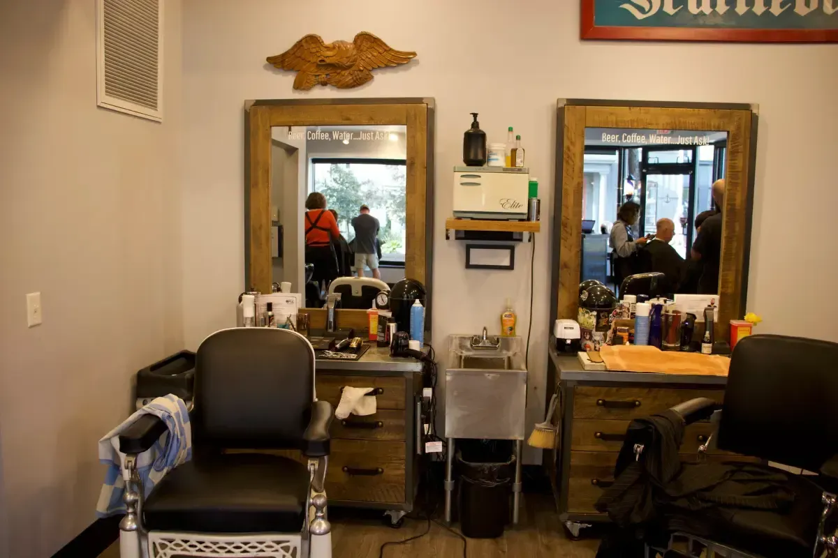 Interior of Scuttlebutt Barbershop with barber chairs, mirrors, and a barber working with a client in the reflection