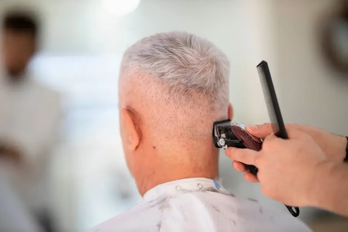 Barber giving a haircut with clippers to a man with short gray hair