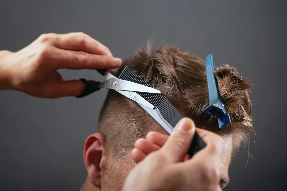 Barber cutting a man’s hair with scissors and comb during a trim