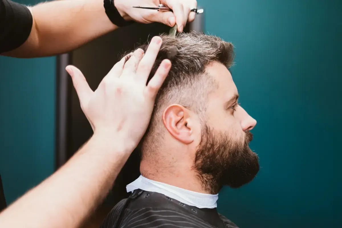 Barber cutting a man’s hair with scissors during a trim